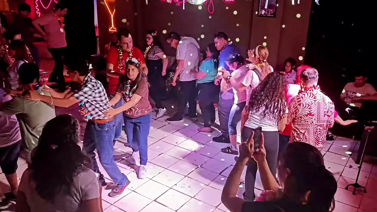 Toma amplia de la pista de baile de la Fiesta de las Flores: personas con collares de flores bailan bajo luces de colores